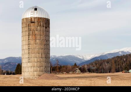 Un vieux silo en béton sur une ferme, près de Iron Creek, à l'extérieur de Troy, Montana. Sommets enneigés de la chaîne de montagnes Cabinet au loin. Banque D'Images