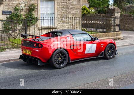 Un Lotus Elise rouge vif, avec des panneaux de numérotation blancs sur les portes, en traversant le village de Yatton Kennel dans le Wiltshire près du château de Coombe Banque D'Images