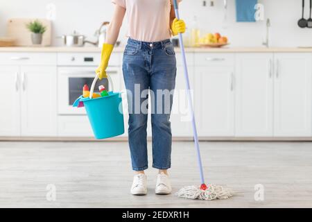 Jeune femme méconnaissable avec seau de produits de nettoyage et balai prêt à essuyer le sol de la cuisine, à l'intérieur Banque D'Images