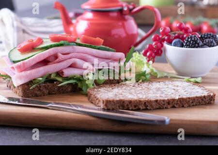 Petit déjeuner-sandwich ouvert sur une table de cuisine avec théière et baies fraîches Banque D'Images