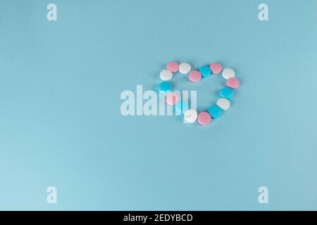 Médicaments et pilules. Pilules bleues, roses et blanches en forme de cœur. Médicaments multicolores sur fond bleu pastel. Banque D'Images