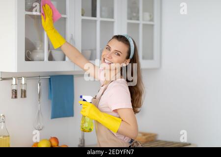 Une femme de ménage positive qui tirait un appartement moderne, essuyant la cuisine cabinat avec un détergent et un chiffon Banque D'Images