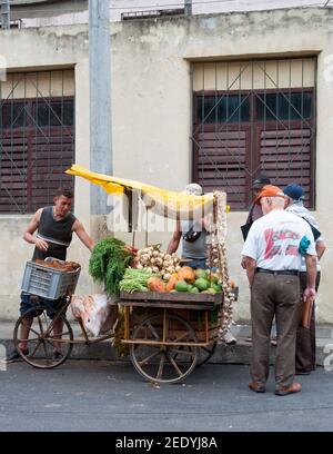 Un homme qui vend des légumes sur un chariot de tricycle au bord de la route Dans la rue pendant que les gens regardent les légumes sur le chariot Banque D'Images