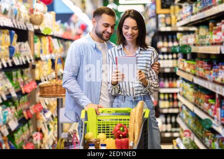 Jeune couple lisant la liste de shopping dans le supermarché Banque D'Images