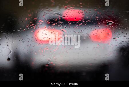 Bielefeld, Allemagne. 15 février 2021. Les gouttes de pluie se trouvent sur le pare-brise d'une voiture, tandis que les feux stop sont visibles sur le véhicule qui se trouve devant. La pluie et la boue entravent la circulation routière dans de grandes parties de la Rhénanie-du-Nord-Westphalie. Lorsque la température est proche du point de congélation, des routes glissantes peuvent se produire. Credit: Friso Gentsch/dpa/Alay Live News Banque D'Images