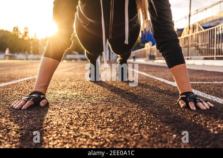 Jeune femme athlétique faisant de l'exercice de planche sur la piste de course à pied. Coucher de soleil sur fond, belle perspective. Banque D'Images