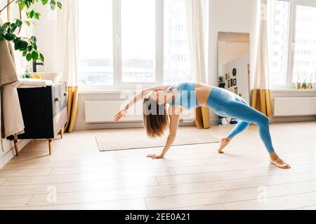 Portrait d'une belle jeune femme pratiquant le yoga à l'intérieur. Femme de sport bleu pratique la posture sauvage à la maison légère. Banque D'Images