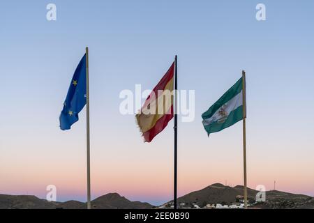 Les drapeaux de l'Union européenne et de l'Espagne et de l'Andalousie au coucher du soleil avec des collines de prairies désertiques derrière Banque D'Images