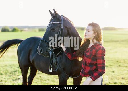 Jeune fille debout à côté d'un beau cheval sombre. Amitié. Équitation. Banque D'Images