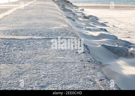 Rive de la mer avec sable blanc fin se déplaçant à travers le blizzard sur une route tarmac Banque D'Images