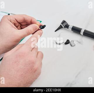 Traitement de la surdité pour les gens. ORL médecin tenant une prothèse auditive intra-auriculaire dans les mains. De nombreux types d'appareils auditifs et d'otoscope sont sur la table Banque D'Images