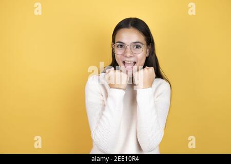 Belle enfant fille portant des vêtements décontractés très heureux et excités faisant le geste gagnant avec les bras relevés, souriant et criant pour le succès. Banque D'Images