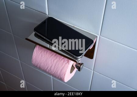 Téléphone portable dans les toilettes avec papier toilette rose contre blanc fond de mosaïque .addiction de concept au téléphone Banque D'Images