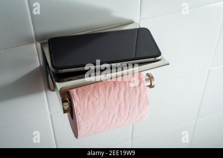 Téléphone portable dans les toilettes avec papier toilette rose contre blanc fond de mosaïque .addiction de concept au téléphone Banque D'Images