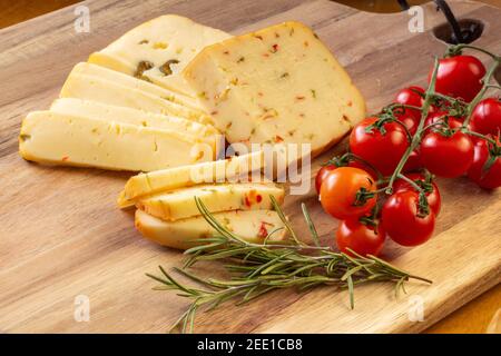 Fromage doux aux olives et fromage aux piments avec tomates et romarin - fond en bois Banque D'Images