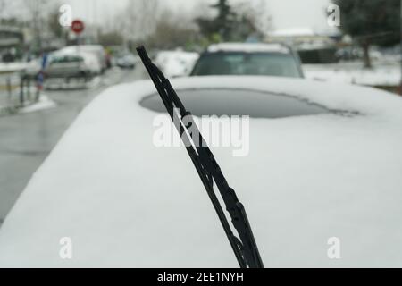 Soulevez l'essuie-glace avant d'avoir recouvert une voiture de neige. Vue de jour de la lame de pare-brise gelée relevée sur un fond flou d'un véhicule en stationnement par temps froid d'hiver. Banque D'Images