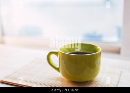 tasse verte avec café sortant de la fumée reposant sur un bois avec un fond fluide et ensoleillé. Banque D'Images