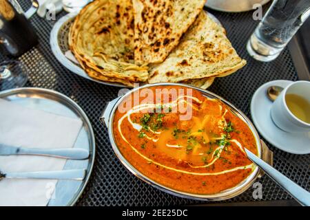 Tikka masala de poulet indien épicé dans un bol, une tasse de thé, une assiette de pain naan au beurre, un verre d'eau sur la table du restaurant. Banque D'Images