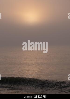 Le soleil levant vu sur la mer depuis la plage sur la côte sud de l'Angleterre, le matin brumeux et brumeux de février. Banque D'Images