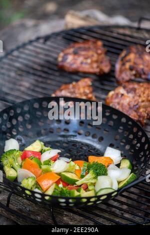 Un panier de légumes et de cuisses de poulet marinées cuisent sur un feu de camp chaud. Repas à l'extérieur. Légumes grillés. Nourriture sur un voyage de camping Banque D'Images