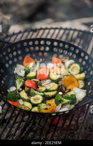 Un panier de légumes et de cuisses de poulet marinées cuisent sur un feu de camp chaud. Repas à l'extérieur. Légumes grillés. Nourriture sur un voyage de camping Banque D'Images