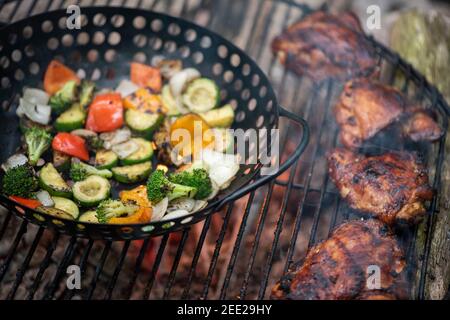 Un panier de légumes et de cuisses de poulet marinées cuisent sur un feu de camp chaud. Repas à l'extérieur. Légumes grillés. Nourriture sur un voyage de camping Banque D'Images
