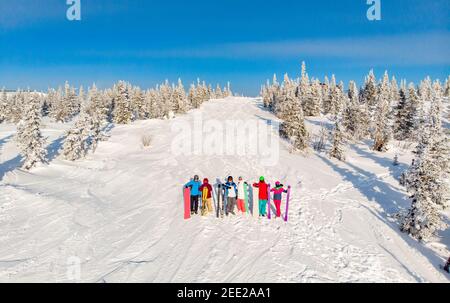 Six amis de skieurs et de snowboarders se tiennent sur la montagne en arrière-plan de la station de ski, se prépare à descendre la pente au milieu de la neige et de la forêt. Antenne Banque D'Images