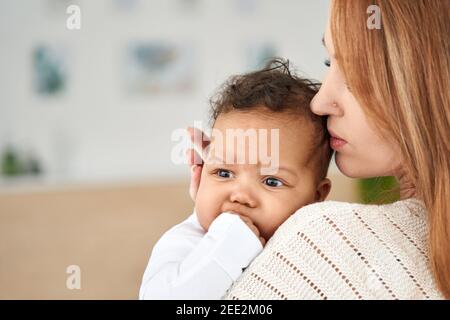 Amour jeune mère apaisant mignon bébé fille dentition main mordant. Banque D'Images