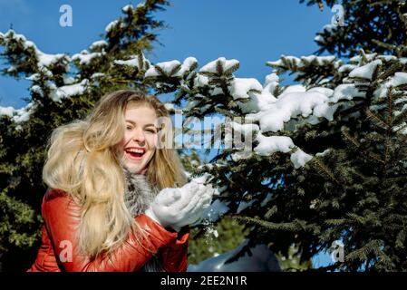 Une fille aux yeux bleus émotionnels soufflant de la neige dans ses mains. Hiver gelé. Banque D'Images