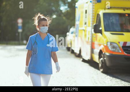 pandémie de coronavirus. femme paramédique moderne dans des exfoliations avec stéthoscope et masque médical marchant à l'extérieur près de l'ambulance. Banque D'Images