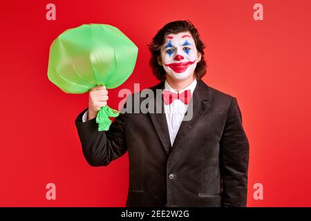 mystérieux magicien tenant un ballon gonflé dans les mains sur fond rouge, magicien en costume noir effectuant des tours Banque D'Images