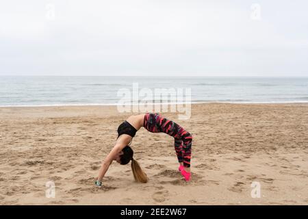 Fitness athlétique femme pratiquant la pose de roue , chakrasana ou urdhva dhanurasana .Femme portant des vêtements de sport s'entraînant, à la plage, en plein air lifesyl Banque D'Images