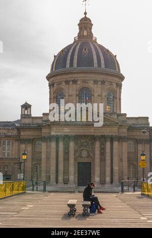 Paris, France - 02 12 2021 : une femme assise sur un banc au Pont des Arts et à la Bibliothèque Mazarine Banque D'Images