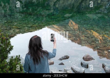 Bloguer de voyage jeune femme debout sur le bord du lac et faire des photos avec son smartphone. Banque D'Images