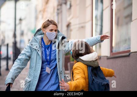 Femme travailleuse de soins de santé à l'extérieur dans la ville rencontre fille d'école, coronavirus concept. Banque D'Images