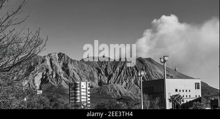 Le cratère fumeur du volcan Sakurajima vu du centre ville de Kagoshima, en noir et blanc. Banque D'Images