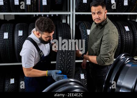 le vendeur de pneus parle des caractéristiques du produit au client nous sommes venus examiner l'assortiment représenté dans l'atelier de service automobile Banque D'Images