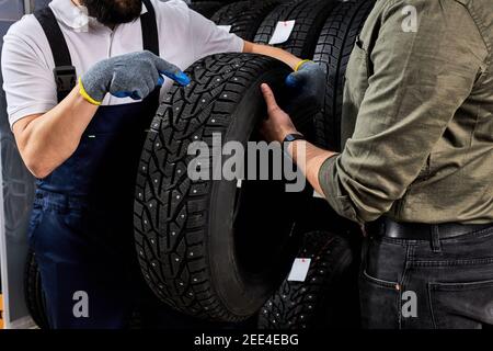 le vendeur de pneus parle des caractéristiques du produit au client nous sommes venus examiner l'assortiment représenté dans l'atelier de service automobile Banque D'Images