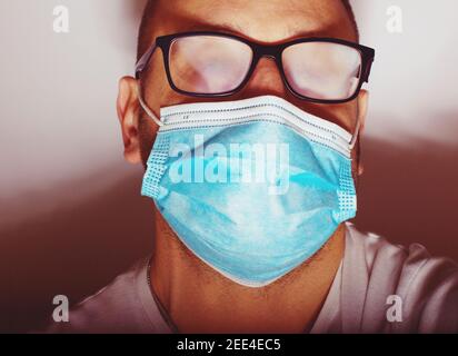 Homme avec des lunettes brumeuses causées par le port d'un masque jetable. Mesure de protection en cas de pandémie de coronavirus Banque D'Images