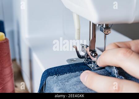 les mains d'une étudiante en design de mode utilisant ses outils universitaires. machine à coudre domestique et électronique. couture d'un jean denim. Banque D'Images