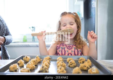 Une petite fille léchant la cuillère tout en faisant cuire des biscuits Banque D'Images