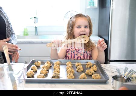 Une petite fille léchant la cuillère tout en faisant cuire des biscuits Banque D'Images