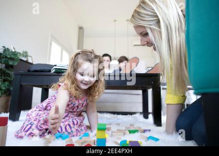 Une mère ou un aidant joue avec une petite fille sur le sol d'une maison moderne. Banque D'Images