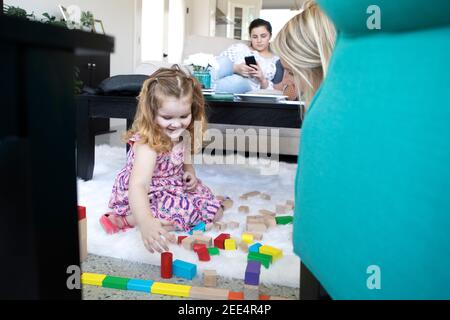 Une mère ou un aidant joue avec une petite fille sur le sol d'une maison moderne. Banque D'Images