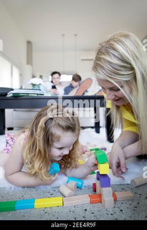 Une mère ou un aidant joue avec une petite fille sur le sol d'une maison moderne. Banque D'Images