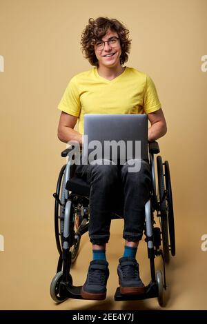 homme handicapé étudiant se préparant à l'examen avec un ordinateur portable, assis sur un fauteuil roulant isolé en studio. portrait. éducation en ligne pour les personnes handicapées Banque D'Images