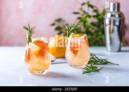 Cocktail Tequila ou limonade froide au jus de pamplemousse, teinté de l'arôme d'une branche fraîche de romarin sur fond rose pastel à la mode. Banque D'Images