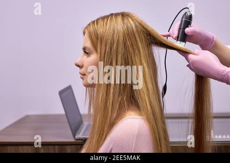 Trichocopie-ordinateur de diagnostic à la cliente femelle par cosmetologiste professionnel, vue latérale sur la vérification de l'état et de la structure des cheveux en utilisant m spécial Banque D'Images