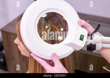 la trichologiste féminine examine l'état des cheveux faibles sur la tête du patient avec le dermatoscope, la procédure de beauté. photo de gros plan de l'équipement Banque D'Images