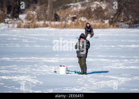 Zegrze, Pologne - 13 février 2021 : pêche sous la glace. Pêcheur à la ligne sur un lac gelé. Sports d'hiver. Les gens sur la glace. Banque D'Images